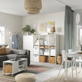 Sala de estar moderna con tonos neutros, con una unidad de almacenamiento blanca VIHALS con estantes y cajones, sofá gris, alfombra colorida y decoración natural.