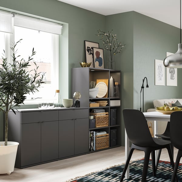 Comedor moderno con muebles grises VIHALS, sillas negras, paredes verdes, planta y decoración.