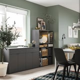 Comedor moderno con muebles grises VIHALS, sillas negras, paredes verdes, planta y decoración.