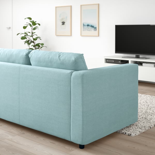 Moderno sofá VIMLE azul en sala de estar minimalista con tv, planta y arte.