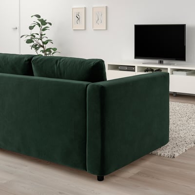 Sala de estar moderna con sofá seccional VIMLE verde oscuro, TV de pantalla plana grande y planta en maceta. El tamaño de los sofás encaja bien con la televisión y la decoración de la pared.