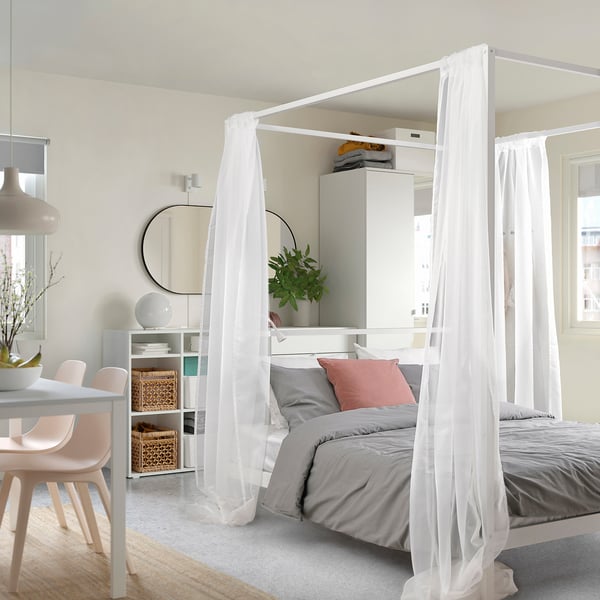 Dormitorio con cama con dosel VITARNA, cortinas transparentes, edredón gris, almohadas rosas. Decoración minimalista, espejo, estanterías, planta.