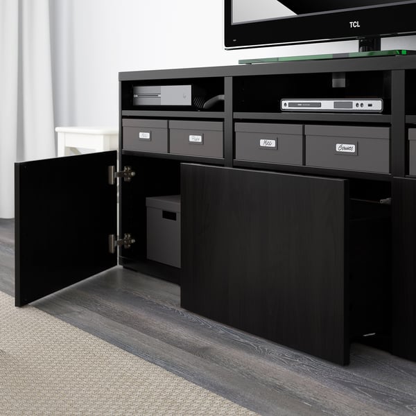 Tv BESTÅ beltzeko altzariak, apal estugarriekin eta biltegiratzearekin. Ate ireki bat, kaxa zuria barruan.