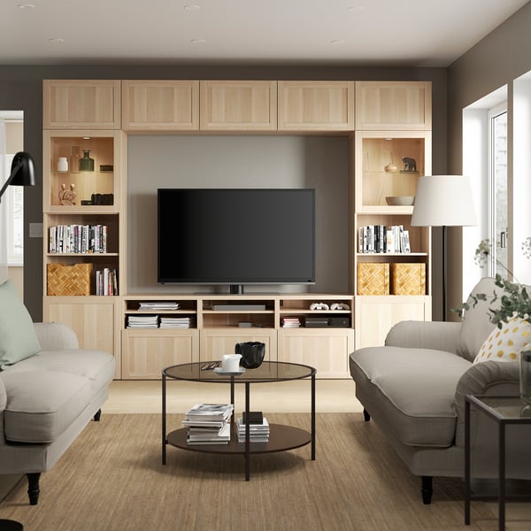 Egongela modernoa, TV BESTÅ beige-ko altzari handiekin, bi sofa gris argi, egurrezko erdiko mahaia, oin beltzeko lanpara eta loreontzidun landarea.