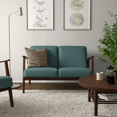 Egongela atsegina sofa berde urdinxkarekin, kafe-mahaia eta aulkia, alfonbra moteatua eta dekorazio-almohadak.