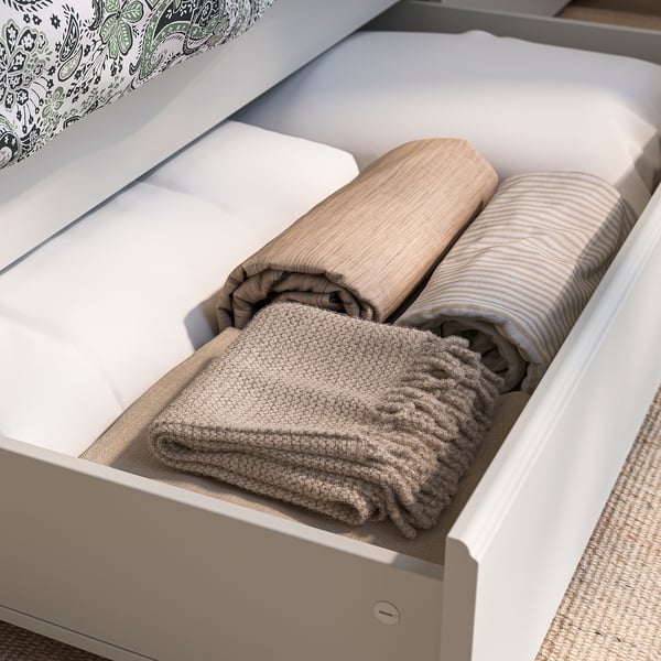 Tiradera irekiak manta tolestuak eta kuxinak erakusten ditu txukun antolatutako ohe-marko batean.