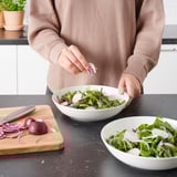 Pertsona bat entsalada prestatzen, FRÖJDEFULL katilu zuriarekin eta egurrezko mozketa taularekin.