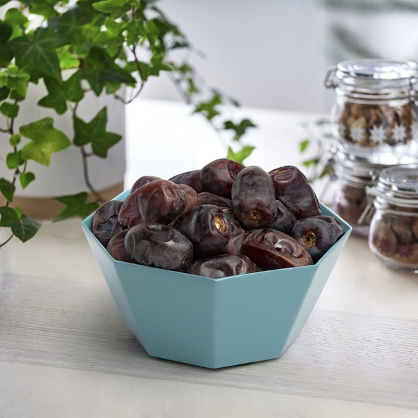 Fruitu lehor ilunez beteta dagoen katilu urdin argi bat, atzealdean landaretza pixka bat duen egurrezko mahai argi baten gainean.