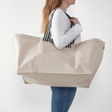 Beige eskuko poltsa handi bat daraman emakumea, erosketak egiteko edo arropa garbitzeko egokia.