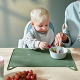 Haurra aulki altuan, katilu bat koilararekin jaten. Silikona berdezko mahai indibidualak mahaia babesten du, katu-diseinua du. Helduen laguntza.