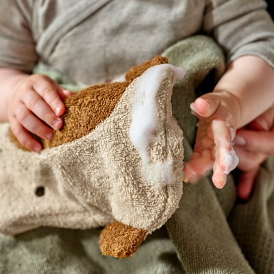 Haurra, GULDVÄVARE jirafa formako beige garbiketako eskularru bati eusten. Kotoi organiko leuna, aurpegi brodatuarekin, garbitasuna leuntzeko egokia.