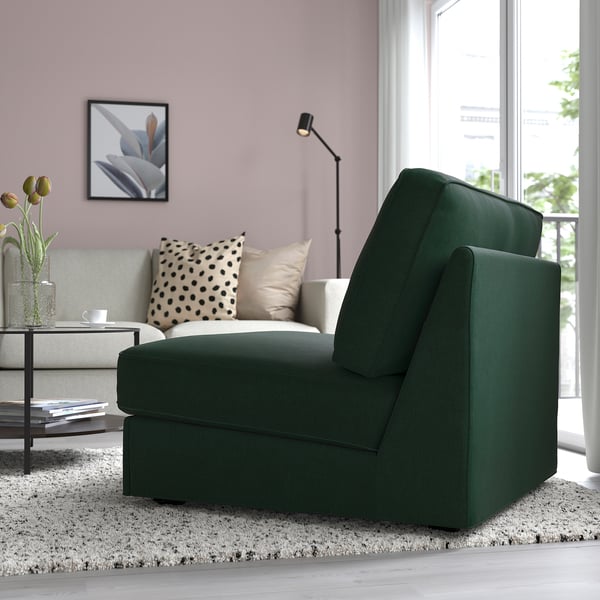 Sofa ohe berde modernoa, horma arrosak, sofa grisa burkoekin, lanpara, apalategia eta leihora begira.