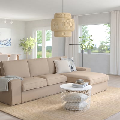KIVIK beige sofa, tumbona sekzionala, lanpara zintzilikari zuria, erdiko mahai dotorea eta leiho handiak dituen egongela modernoa.