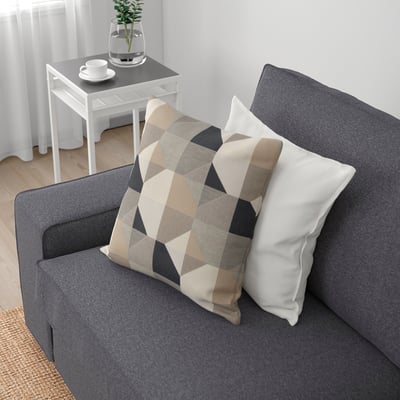 Sofa grisa, burkoak koadro eta zuriekin, landare bat eta te kikara bat dituen mahaitxo baten ondoan.
