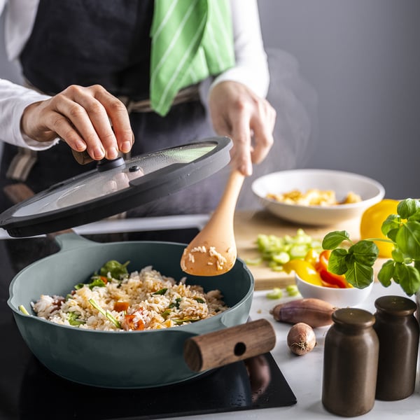 Pertsonak zartaginaren estalkia altxatzen du, eta arroz egosi plater bat erakusten du zartagin gris turkesa batean, egurrezko kirtenarekin berogailu batean. Inguruan, katilu eta belar batzuk daude.