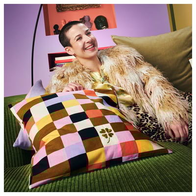 Traje horia eta larruz forratutako jaka dituen pertsona batek irribarre egiten du sofa berde batean, koadrodun zerriarekin.