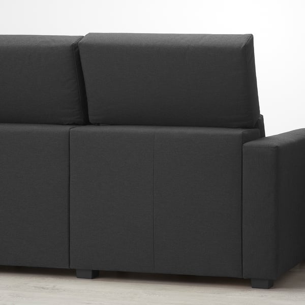 Sofa modularra gris ilunez tapizatua, bizkarralde altuarekin eta hondo zuriaren gainean doi daitezkeen kuxinekin.