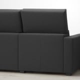 Sofa modularra gris ilunez tapizatua, bizkarralde altuarekin eta hondo zuriaren gainean doi daitezkeen kuxinekin.