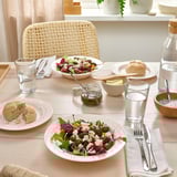 Egurrezko mahai bat, ertz zuria duten platerak, entsalada koloretsuak, opilak, edalontziak eta mahai-tresnak dituena.