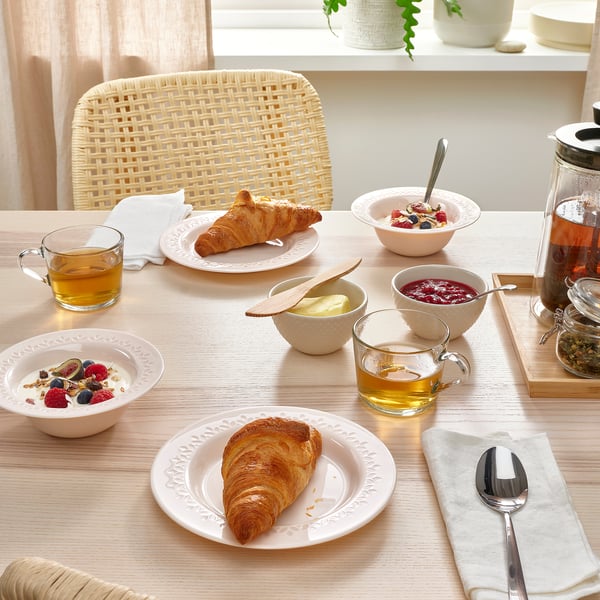 Egurrezko mahaia, bajilla zuriarekin. Fruta kikara, kruasanak, te kikara eta beirazko pitxer bat ditu. Baxera, ertz estanpatua dauka.