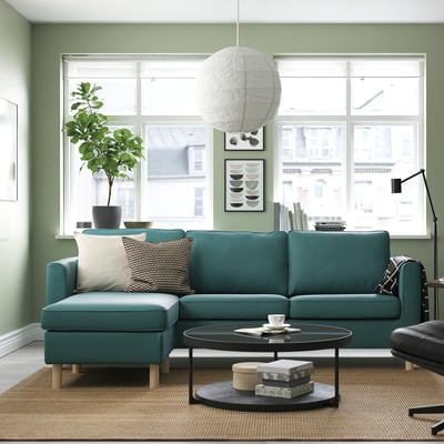 Egongela modernoa sofa berdea, mahai borobila, leiho handiak eta kuxin zabalak dituena.