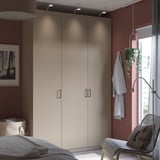 Logela modernoa, PAX beige armairu altua, aulki dotorea, landare berdea, artea eta argi naturala.