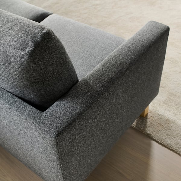Kuxin sendoekin eta egurrezko hanka ikusgaiekin sofa gris moderno baten hurbileko planoa.