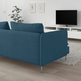 Sofa SÖDERHAMN urdina egongela minimalistan, sakona eta erosoa, chenilla ehuna, hanka altuak. Telebista, landarea, alfonbra jokoan.
