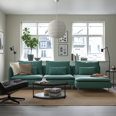 Sofa berde urdinxka duen egongela modernoa, leiho handiak, hirira begira.