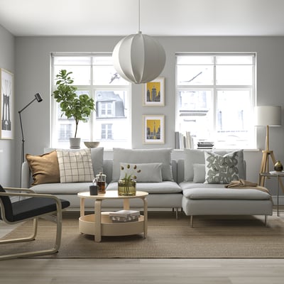 SÖDERHAMN sofa grisak, sakonak, kuxin handiak eta egurrezko mahai borobila, hirira begira zegoen leiho handi baten ondoan.