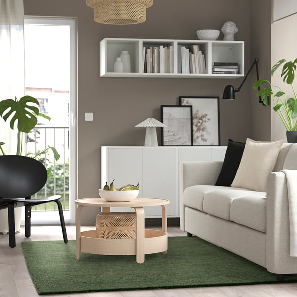 STOENSE berdea, sofa argia, aulki beltza eta landareak dituen egongela modernoa.