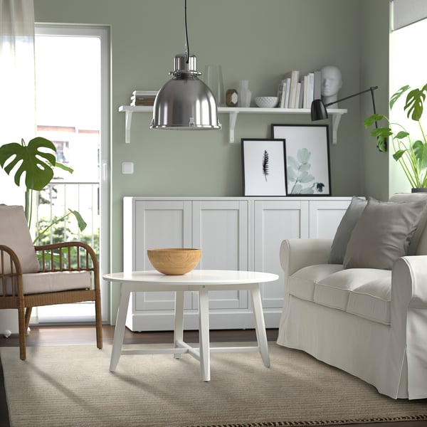 Egongela modernoa horma berdeekin, TßGSPÅR alfonbra zuria, egurrezko erdiko mahaia, sofa grisa, zumezko aulkia eta loreontzietako landareak.