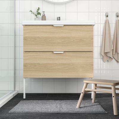 Bainu modernoa, egurrezko apaingailuarekin, beirazko dutxarekin, alfonbra grisarekin, beige taburetearekin eta eskuoihalekin