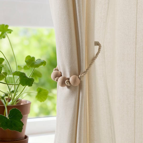 Gortina beige gorbatak leihoan egurrezko perlekin. Sarraila magnetikoek argi-gortinak babesten dituzte. Ondoko landareak.