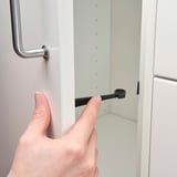 Esku batek armairu beltzeko sarraila bat armairu zuri batekin lotzen du, eta horrek haurren segurtasuna hobetzen du.