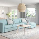 Areto modernoa: sofa VIMLE urdin argia alfonbra zuriaren gainean, egurrezko mahaia, leiho handia, landarea, lanpara.