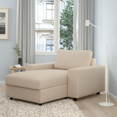 Sofa beige-a biltegiarekin, besa-euskarri zabalekin eta diseinu minimalistarekin, gela argitsu eta abegitsu batean.