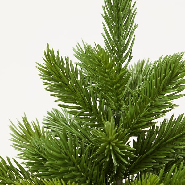 Zuhaitz artifizialeko adar baten lehen planoa, orratz berde errealistak dituena, patroi natural eta trinko batean kokatuta.