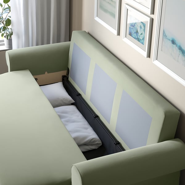 Sofa-ohea, bizkar-kuxinekin, biltegiratzeko espazioa eta lo-eremua erakusten ditu, hormaren kontra jarrita, arte markoztatuta.