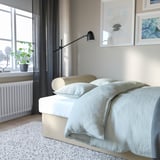 Logela, sofa-ohea VRETSTORP-arekin, estalki urdin argia, lanpara beltzaren azpian, oinplanoa duen leihoaren ondoan.