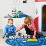 Dous nenos xogando cunha construción de temática espacial AFTONSPARV situada nunha alfombra azul, rodeado de peluches e unha casa de xogos.