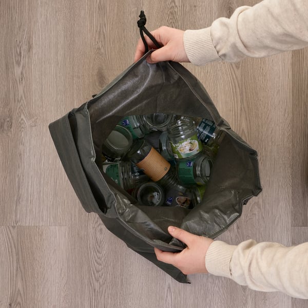 Persoa que sostén unha bolsa de reciclaxe ecolóxica AJÖSS chea de latas e botellas, demostrando o seu uso para a clasificación e transporte de residuos.