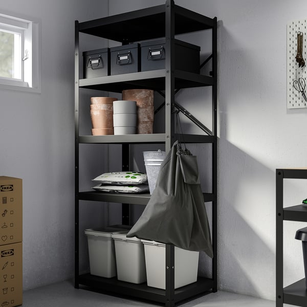 O estante negro de IKEA AJÖSS garda potes, caixas e papeleiras de barro nunha esquina.