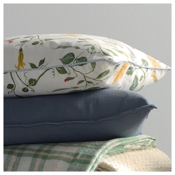 Vista frontal de dúas almofadas apiladas: branco superior con estampado floral verde, abaixo azul, sobre manta texturizada.