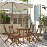 Conxunto de comedor ao aire libre de madeira de acacia marrón ASKHOLMEN con 4 cadeiras plegables e mesa, perfecto para espazos pequenos.