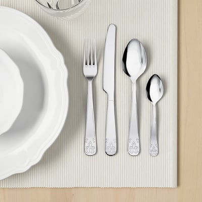 Catro utensilios de prata pulidos - garfo, coitelo, dúas culleres - colocados nunha alfombra branca xunto a unha cunca branca. Ideal para comer elegante.