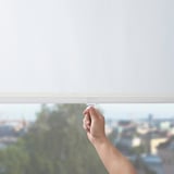 Man baixando unha persiana en un cuarto, revelando unha vista da cidade. A persiana filtra a luz e ofrece privacidade nocturna.