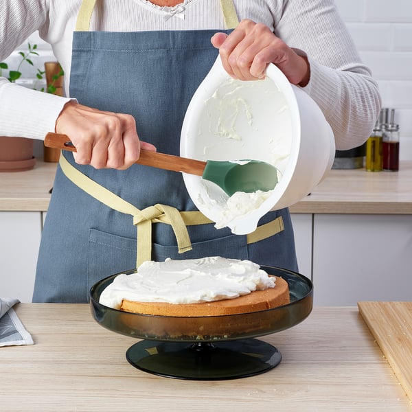 Persoa en mandil espallando xeado de cunca en torta con espátula.