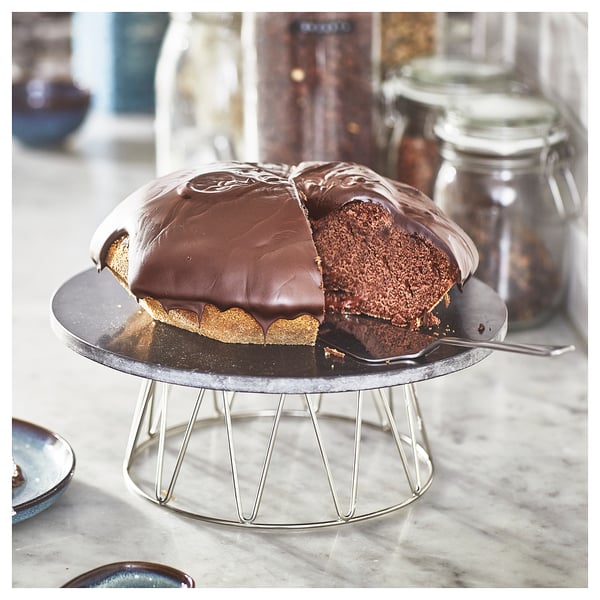 Pequeno soporte de torta con tapa xiratoria de mármore, mostrando torta de chocolate medio comida. Patas metálicas, de cor prata, perfectas para cocer e servir.