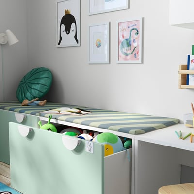 Habitación infantil con almofada de banco BÄNKKAMRAT na cama, almacenando xoguetes; Arte de parede colorida.